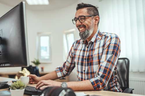 Lächelnder Mann mit Brille arbeitet am Computer in modernem Büro.